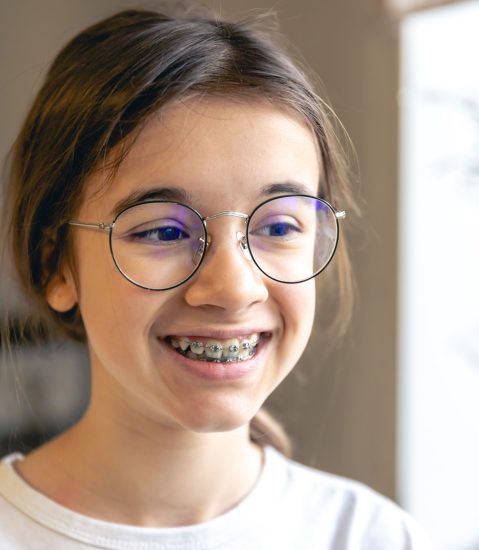 Portrait of a teenage girl with glasses and braces at home. Orthodontic treatment concept.